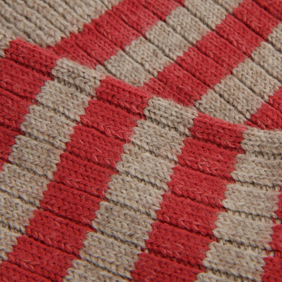 Close-up of a knitted fabric with alternating diagonal stripes in red and beige.