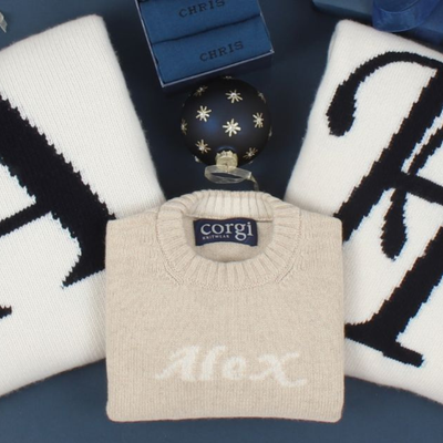 Beige sweater with 'Alex' knitted on it, placed on a dark surface with decorative items.