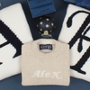 Beige sweater with 'Alex' knitted on it, placed on a dark surface with decorative items.