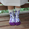 Child wearing white socks with purple mushroom pattern sitting on a wooden bench.