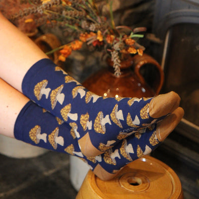 Person wearing dark blue socks with a pattern of white and gold mushrroms, sitting on a wooden stool.