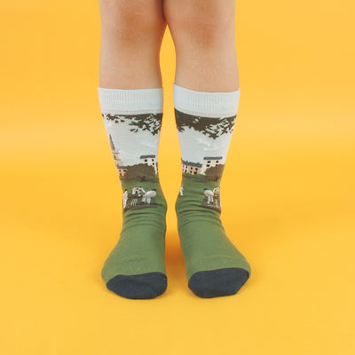 A pair of patterned cotton socks featuring a cricket scene with players on a green field, designed for children.