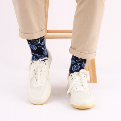 Person wearing navy leaf patterned socks with white sneakers on a light background