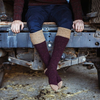 A person seated with Donegal wool welly socks in a colour block pattern, featuring a rustic tweed-effect yarn, in a blue and brown colour scheme.